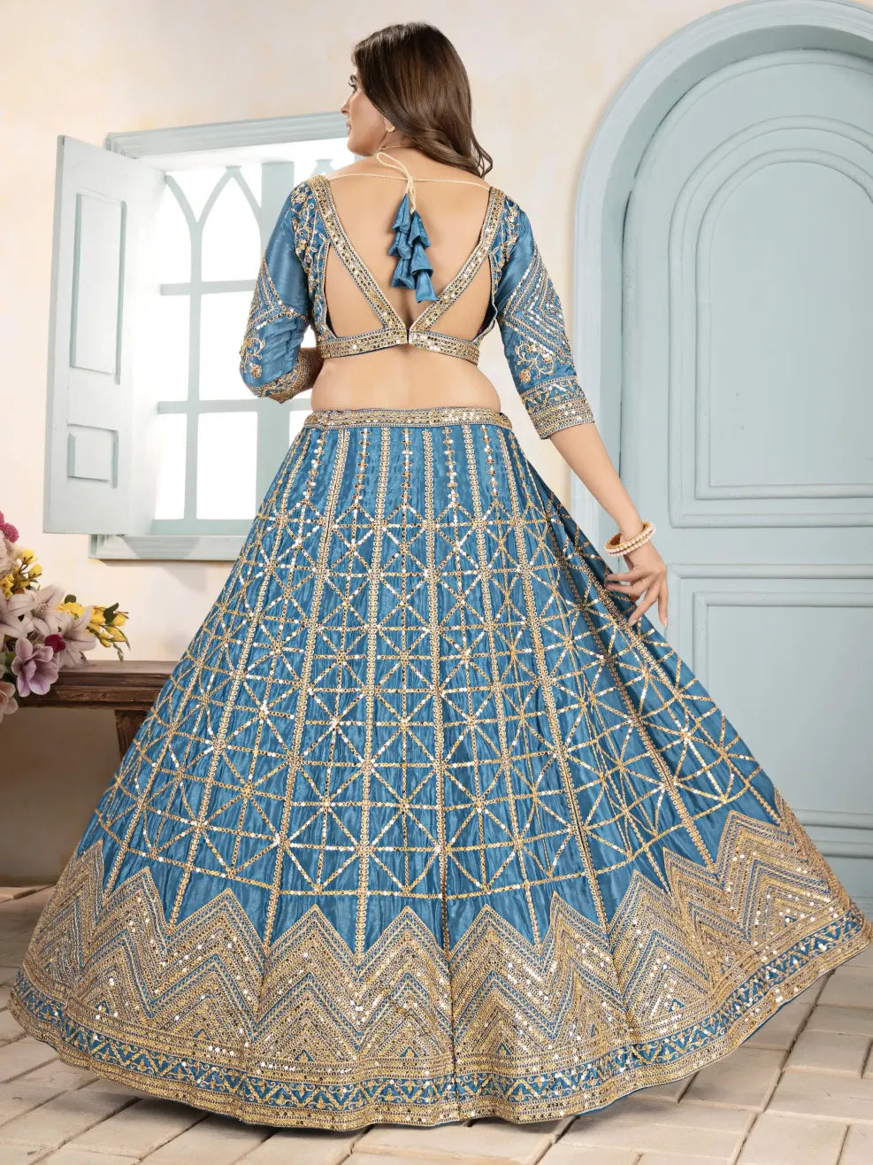 Woman wearing a blue embroidered lehenga with a white door and flowers in the background