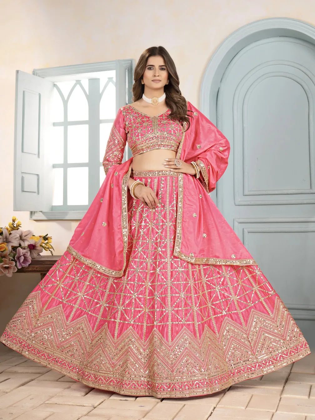 Woman wearing a pink embroidered lehenga in a room with a window and door.