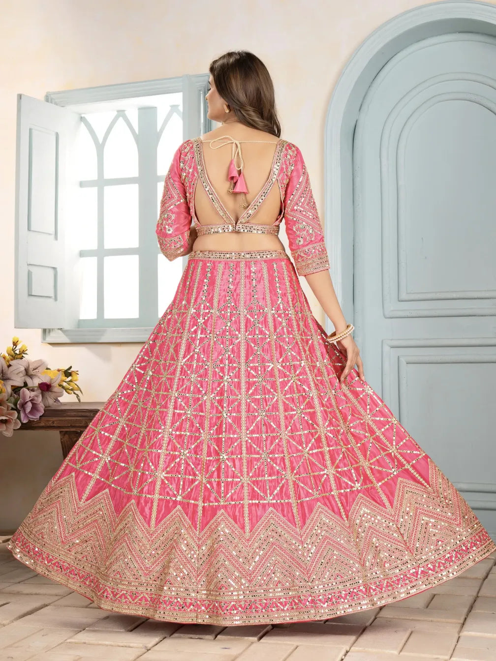 Woman wearing a pink and gold embroidered traditional outfit in a room with light blue walls.