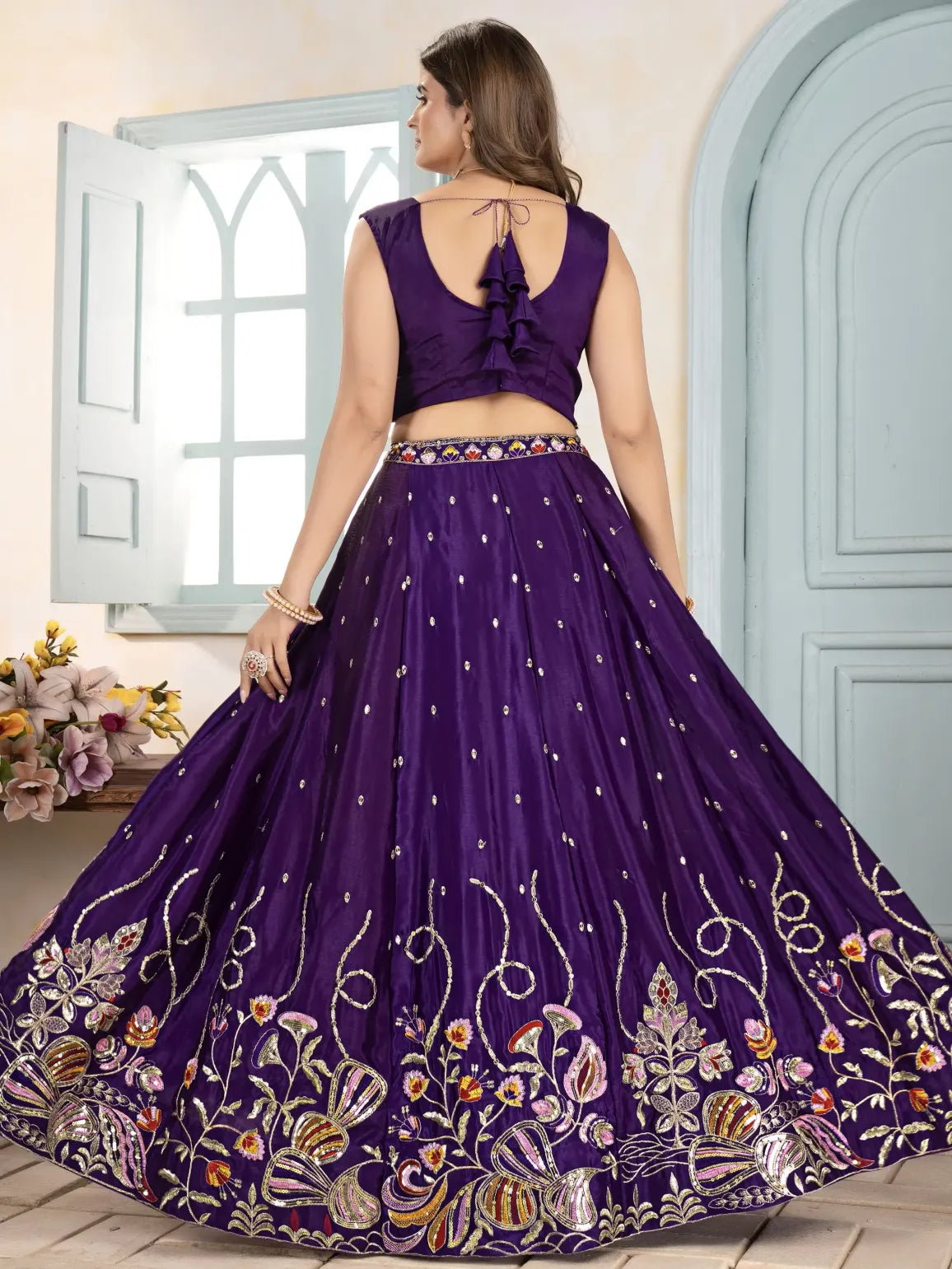 Woman wearing a purple embroidered lehenga in a well-lit room.