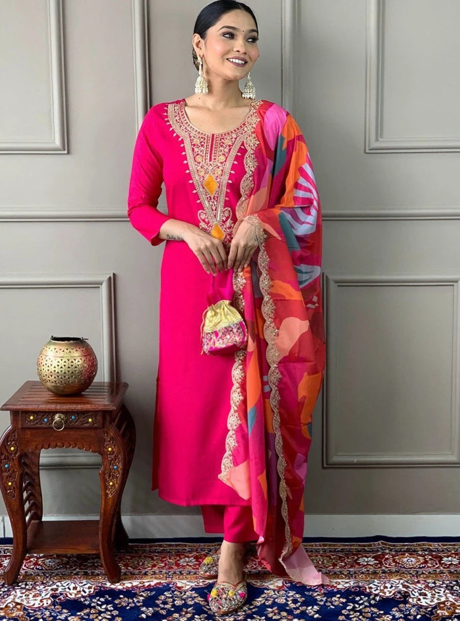 Woman in a bright pink traditional outfit with colorful dupatta against a gray wall.