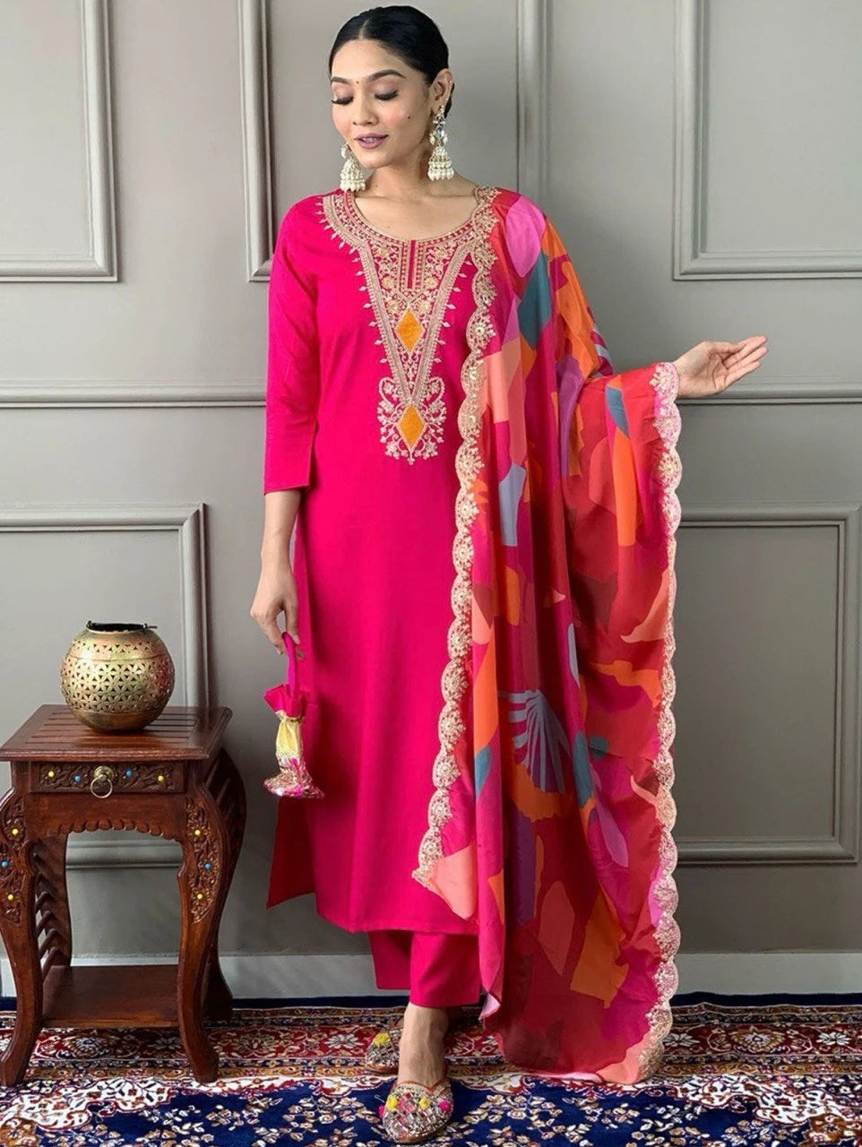 Woman in a bright pink traditional outfit with a colorful dupatta against a gray wall.