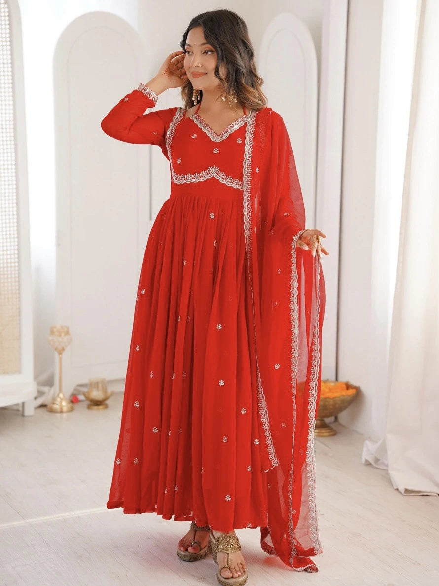 Woman wearing a red dress with white embroidery in a minimalistic room.