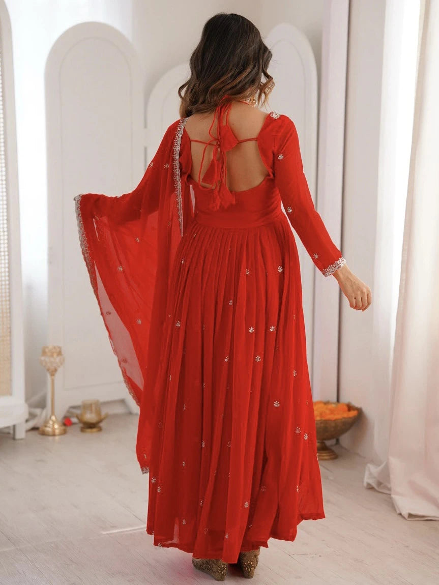 Woman wearing a red dress with a sheer overlay in a bright room.