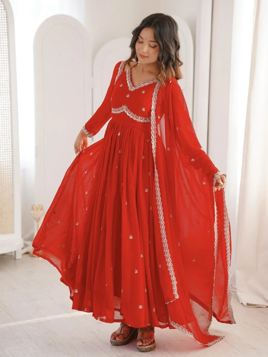 Woman wearing a red traditional outfit with white embroidery in a bright room.