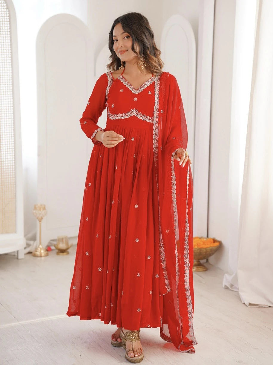 Woman wearing a red traditional outfit with white embroidery in a minimalistic setting.