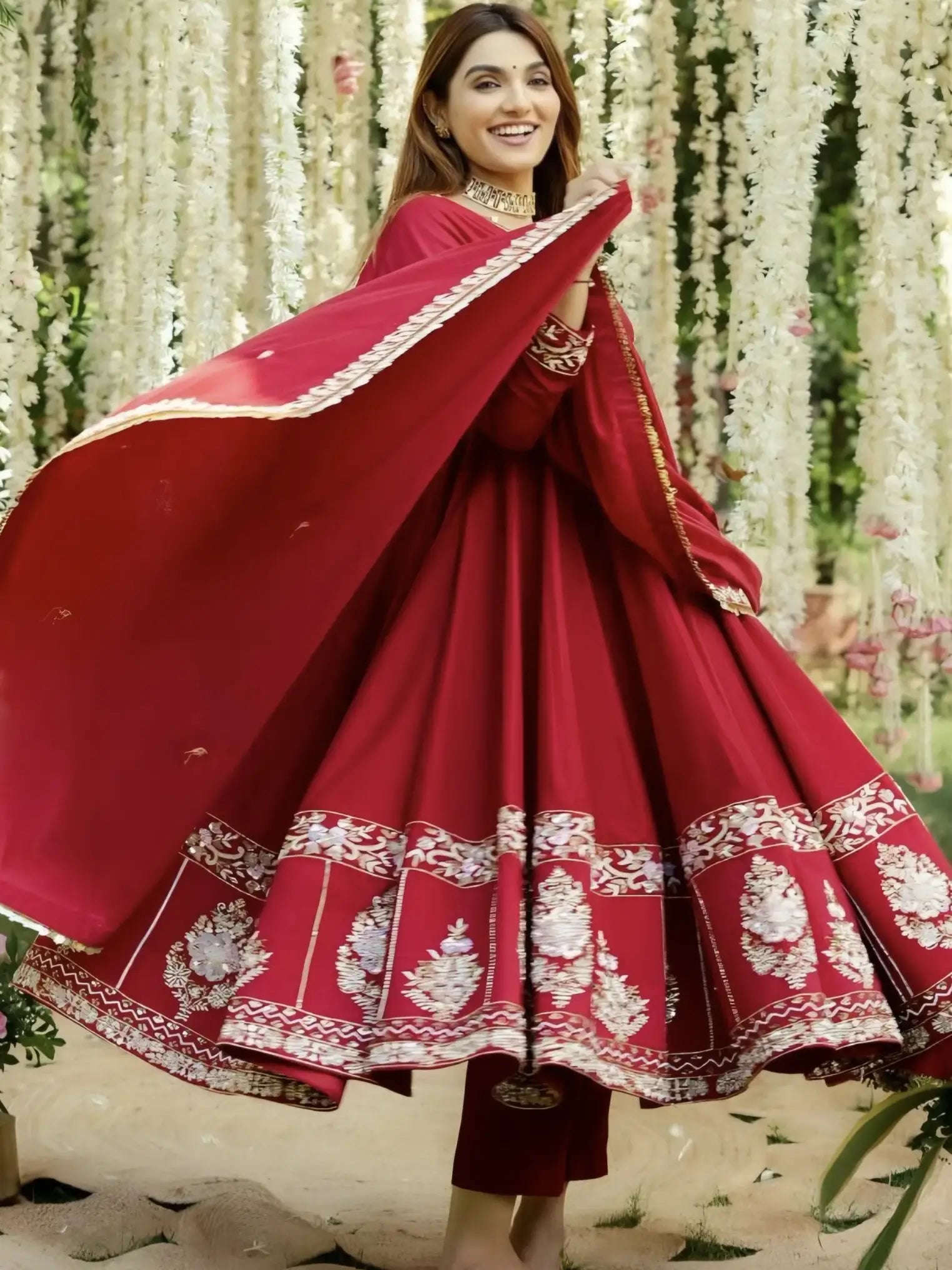 Woman in a red traditional outfit with white embroidery standing in front of floral decorations.