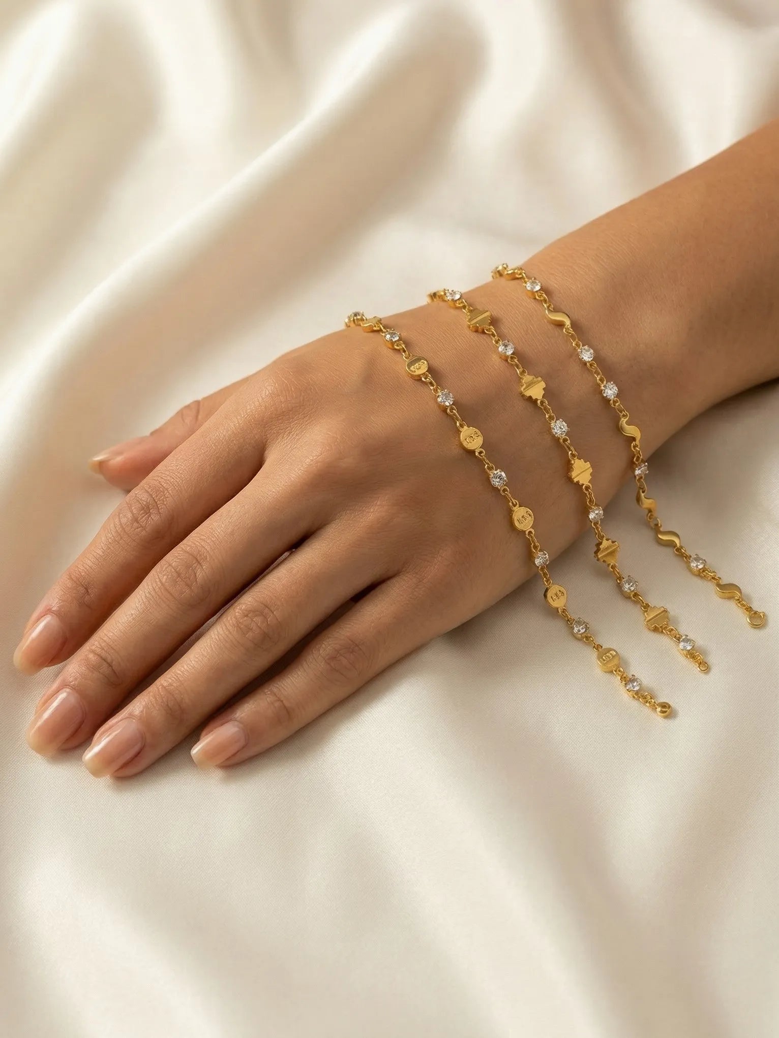 Gold bracelet with floral designs on a hand against a beige fabric background