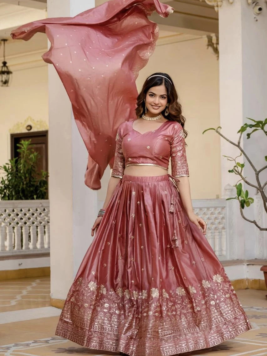 Woman in a traditional pink embroidered outfit standing in an elegant indoor setting.