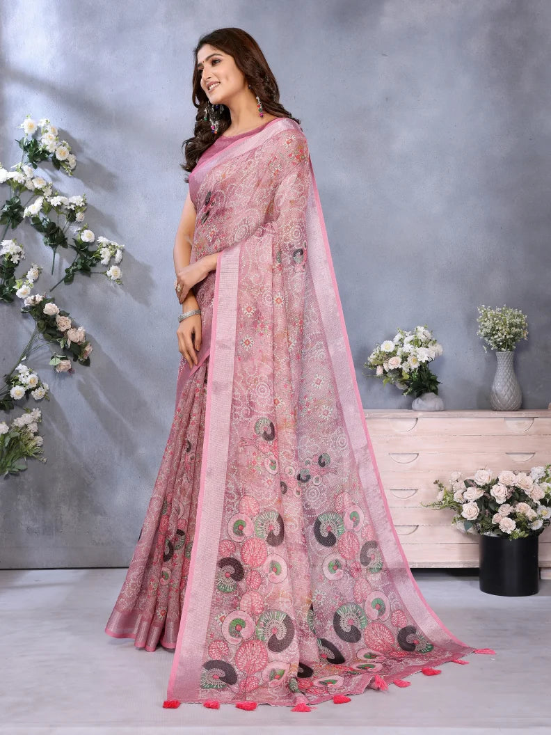 Woman wearing a pink saree with a floral pattern in a decorated indoor setting.