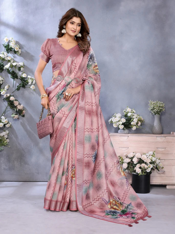 Woman in a pink saree with floral patterns standing against a gray wall with decorative flowers.
