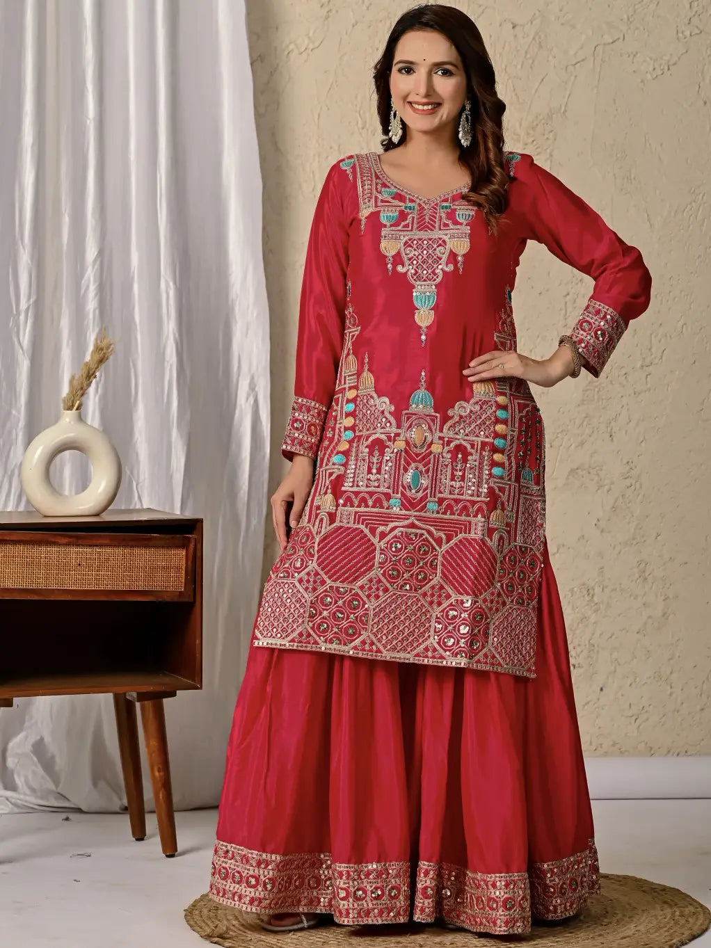 Woman wearing a red embroidered traditional outfit in a room setting.