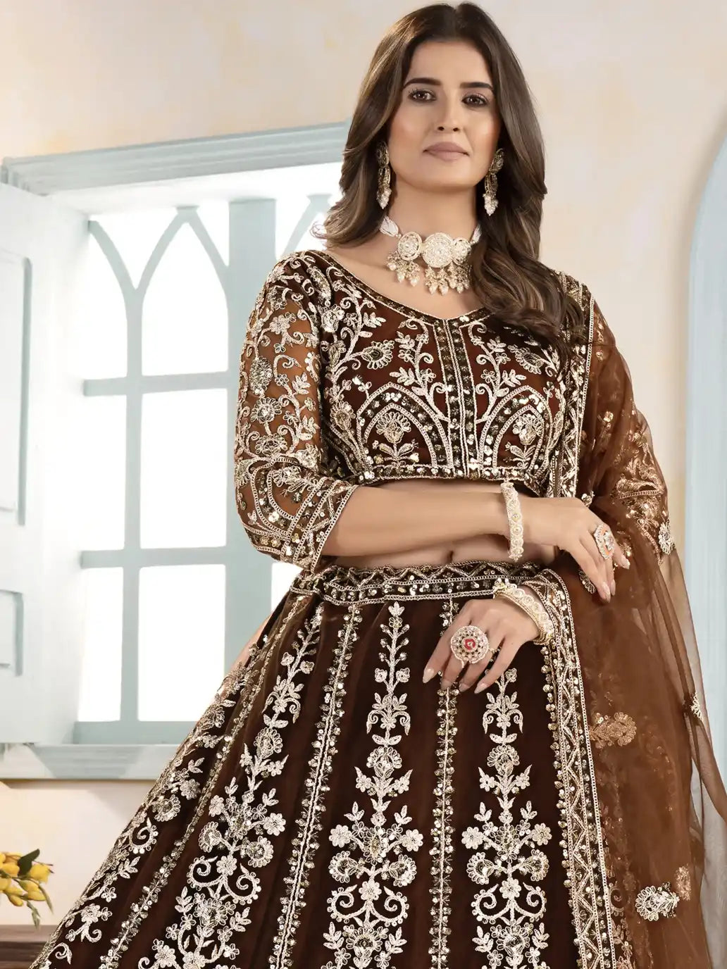 Woman wearing a brown and gold embroidered traditional outfit indoors.