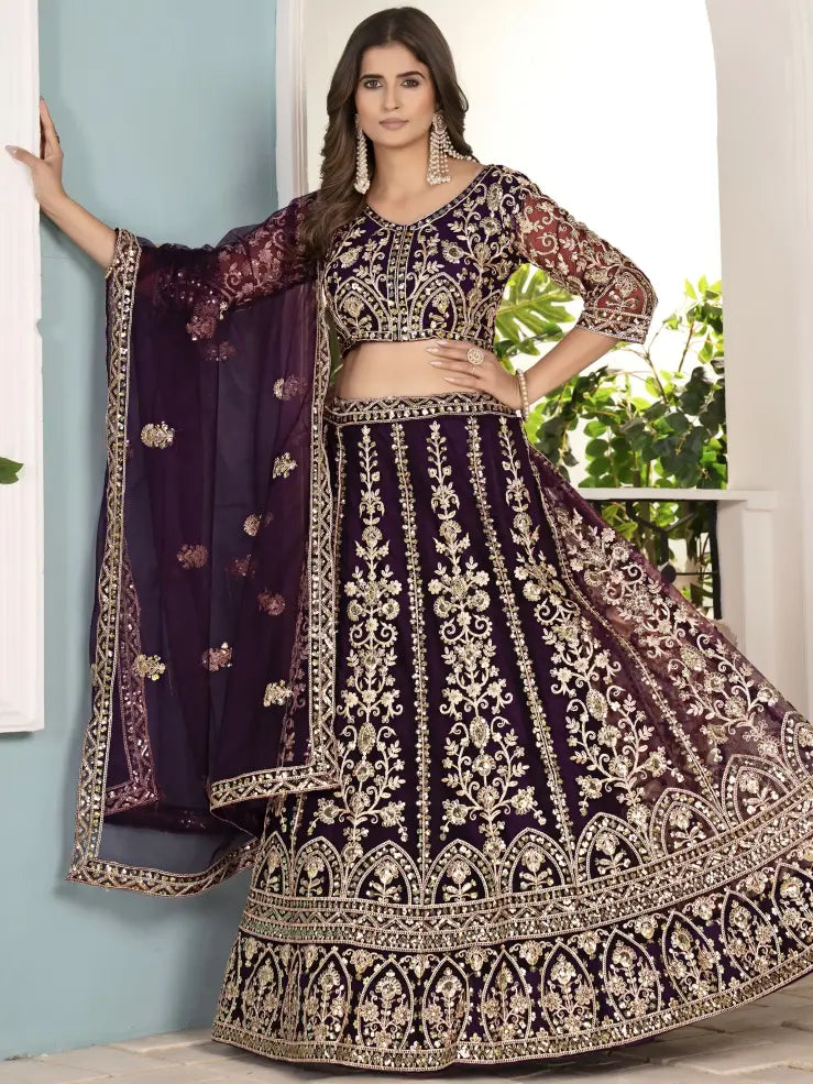 Woman wearing a traditional embroidered outfit with a purple dupatta indoors.