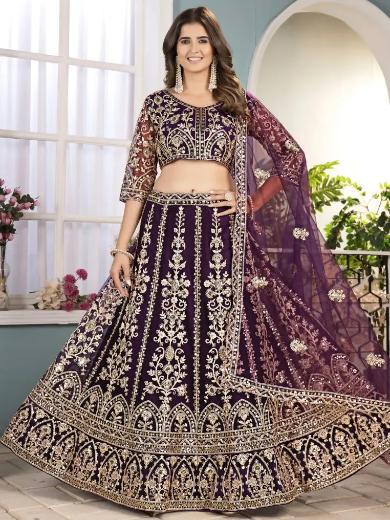 Woman wearing a traditional embroidered purple and gold lehenga in a bright room.