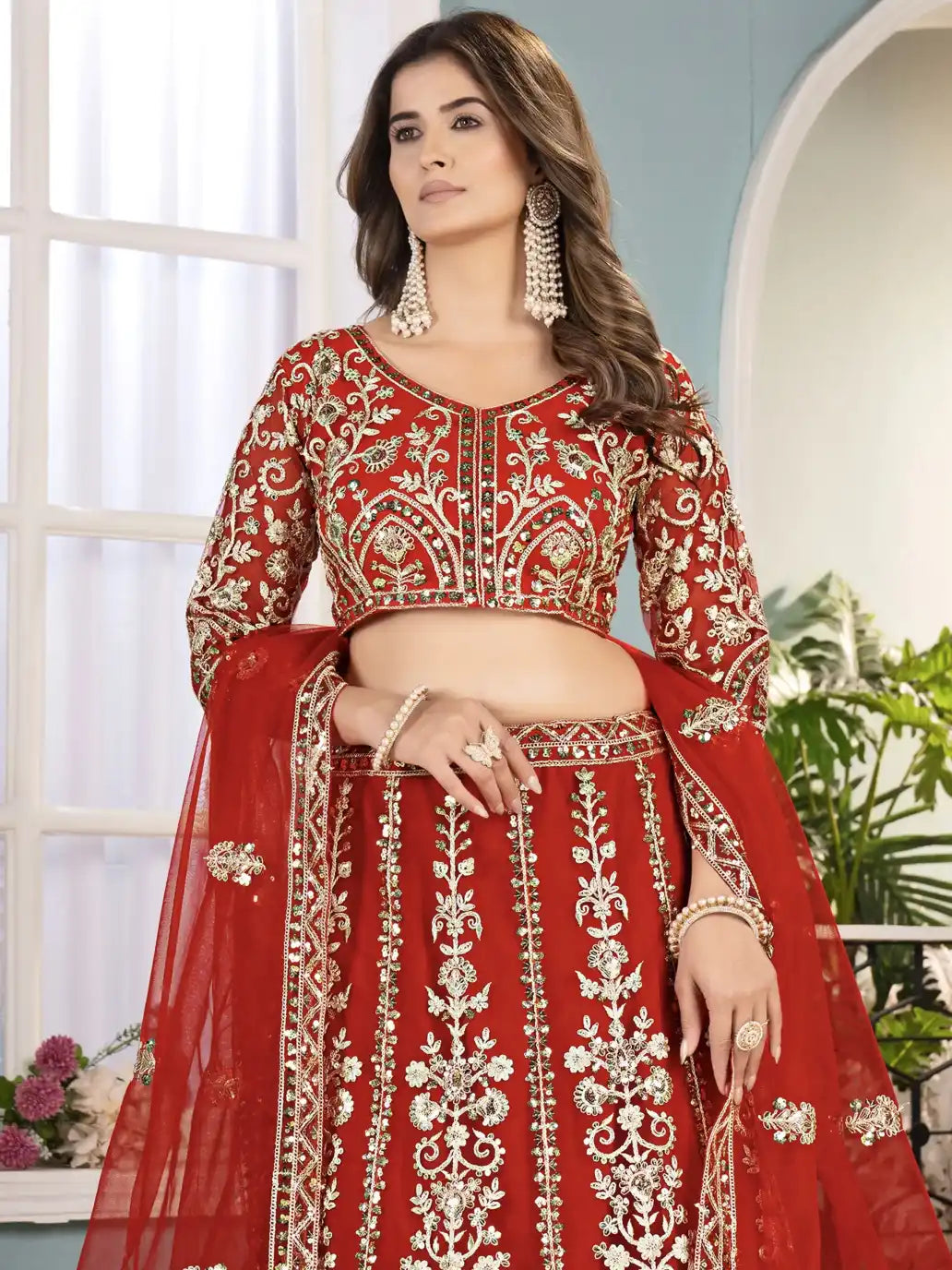 Woman wearing a red embroidered traditional outfit with gold details indoors.