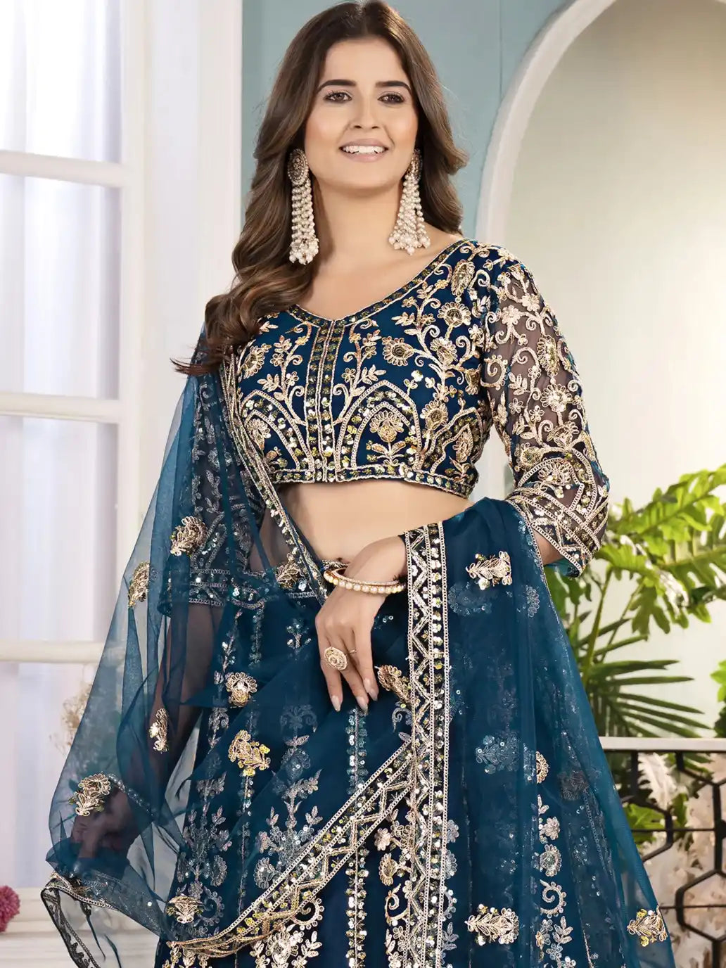 Woman wearing a traditional blue embroidered outfit with gold details indoors.