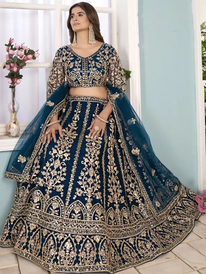 Woman wearing a blue embroidered traditional outfit in a room with light blue walls and white window frames.