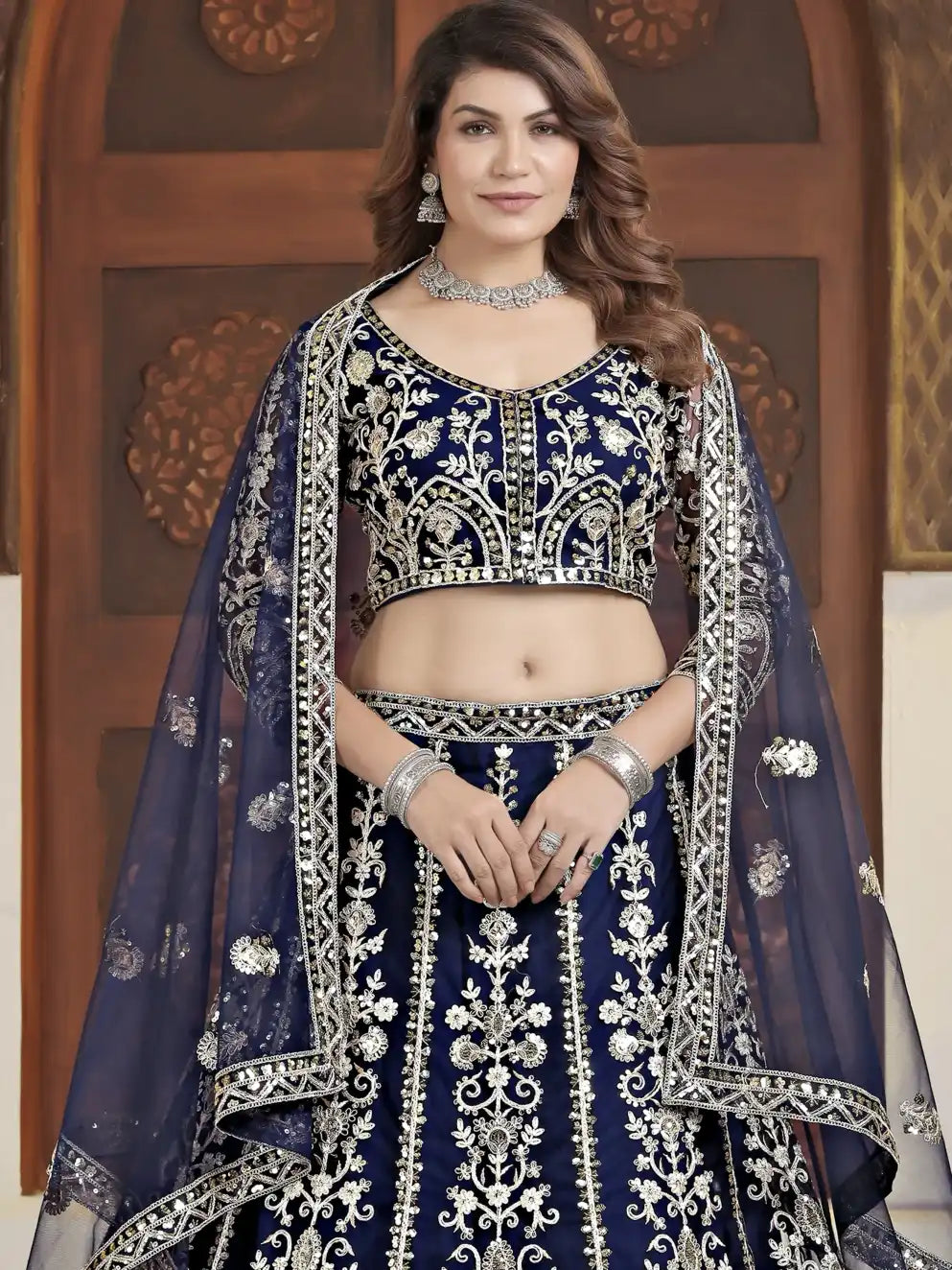 Woman wearing a traditional blue and silver embroidered outfit with a wooden door in the background