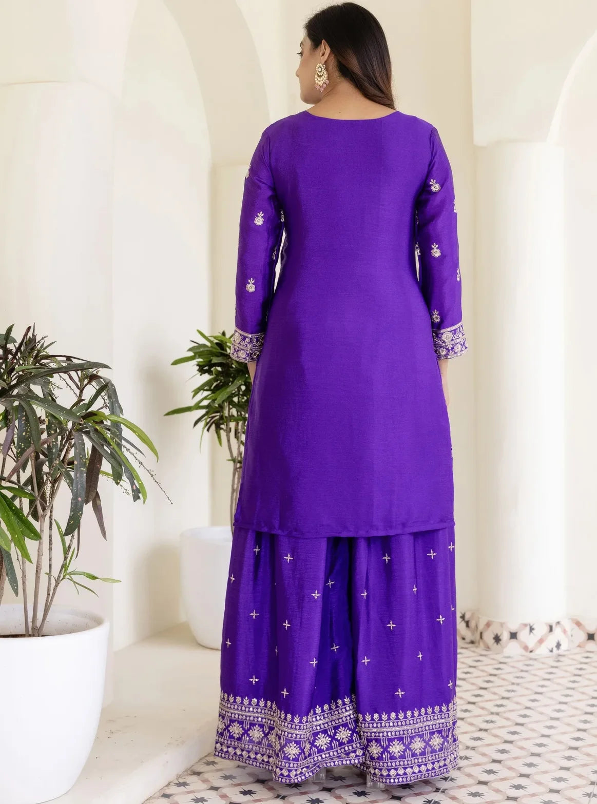 Woman wearing a purple traditional outfit with white patterns in a bright room.