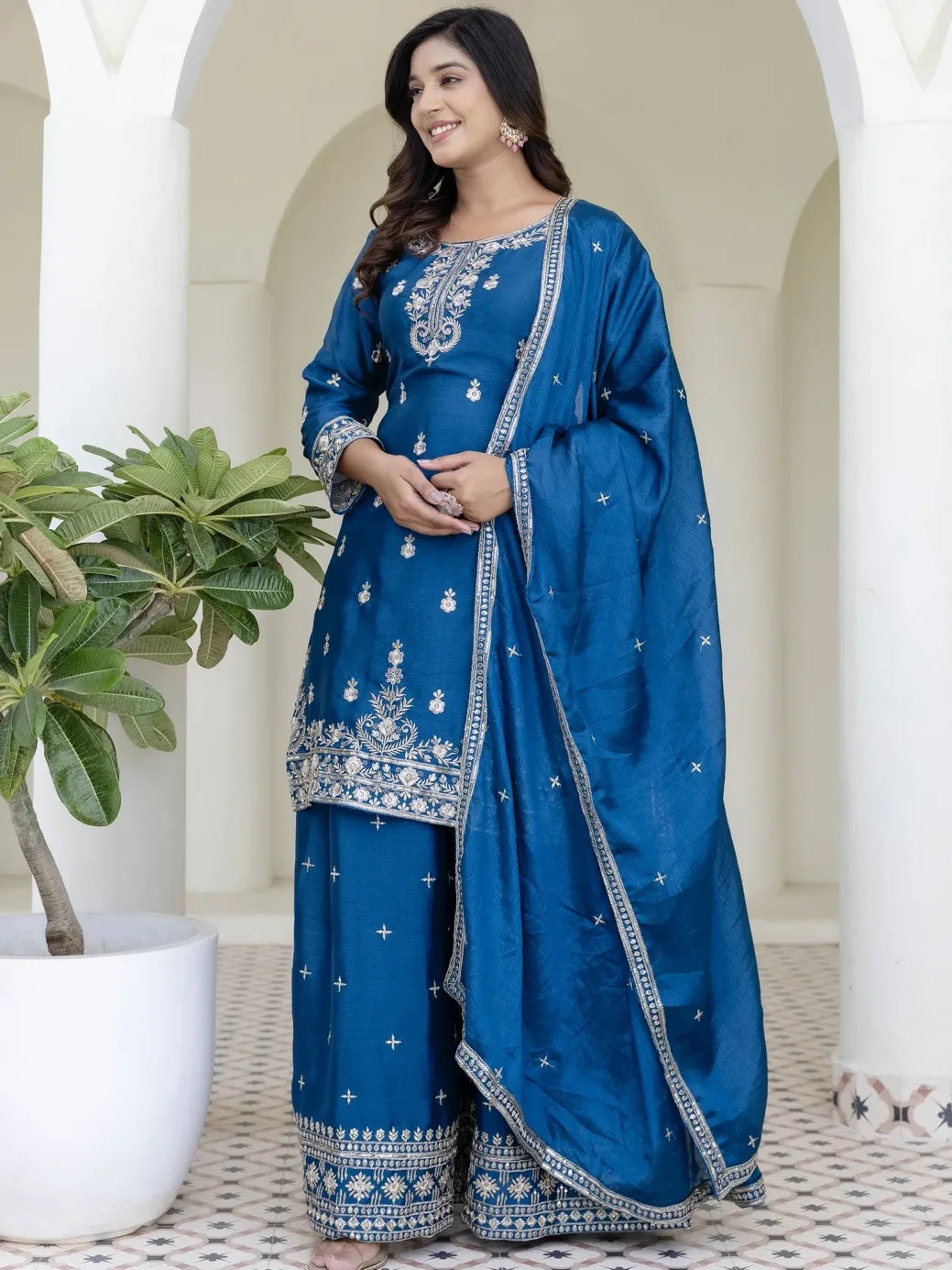 Woman wearing a blue embroidered traditional outfit with a white background