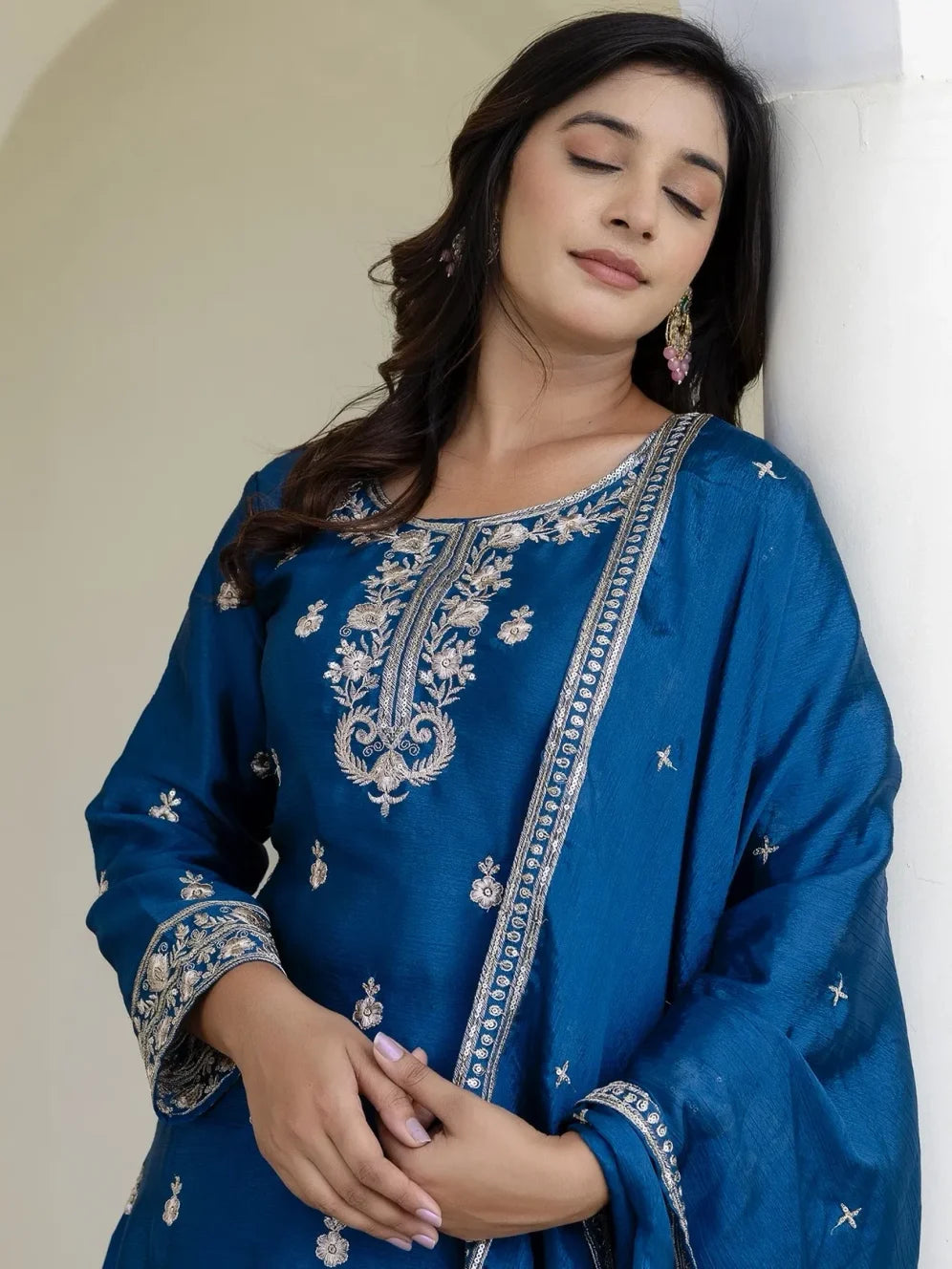 Woman wearing a blue embroidered traditional outfit against a neutral background