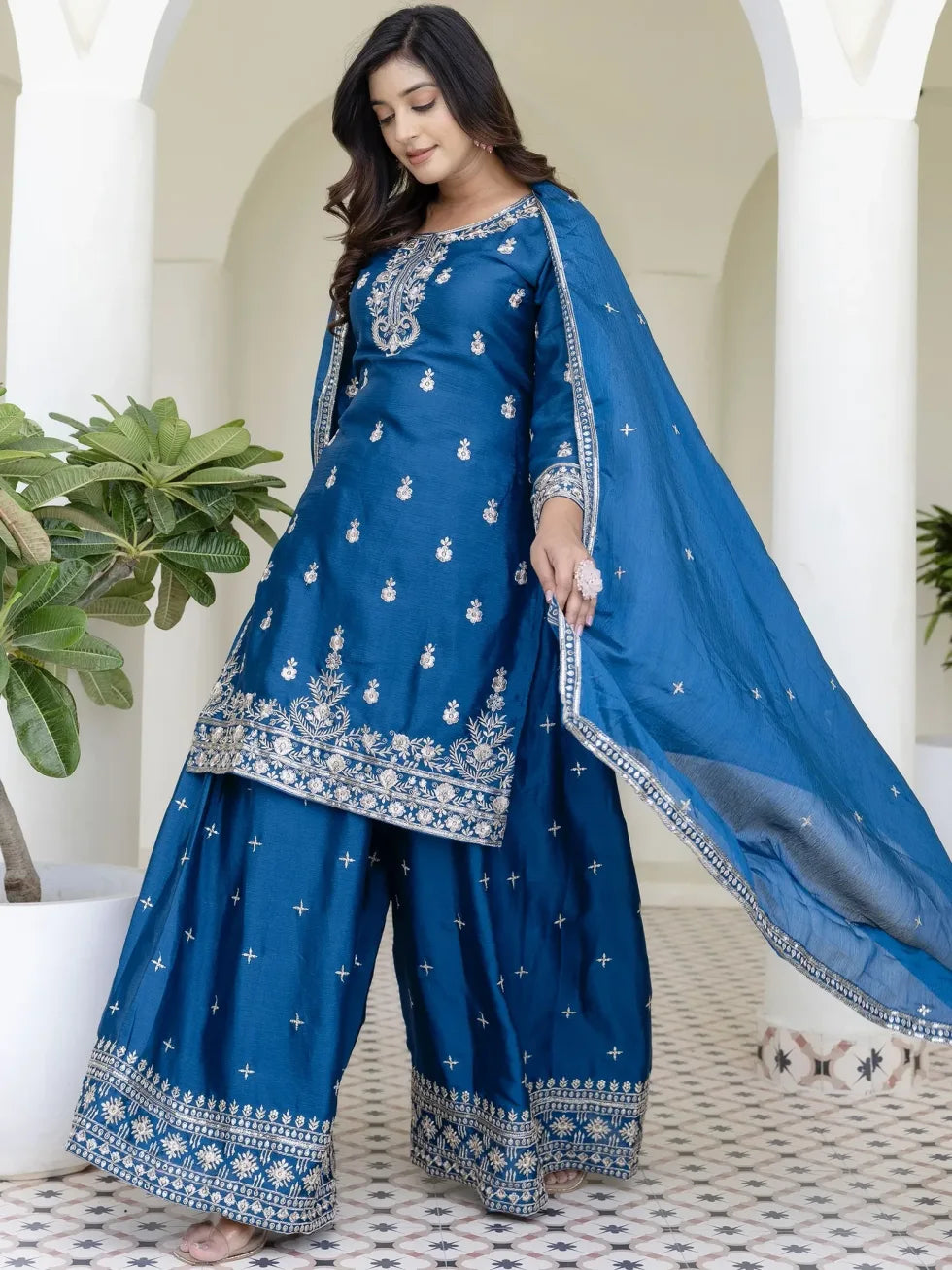 Woman wearing a blue traditional outfit with white embroidery in an outdoor setting.