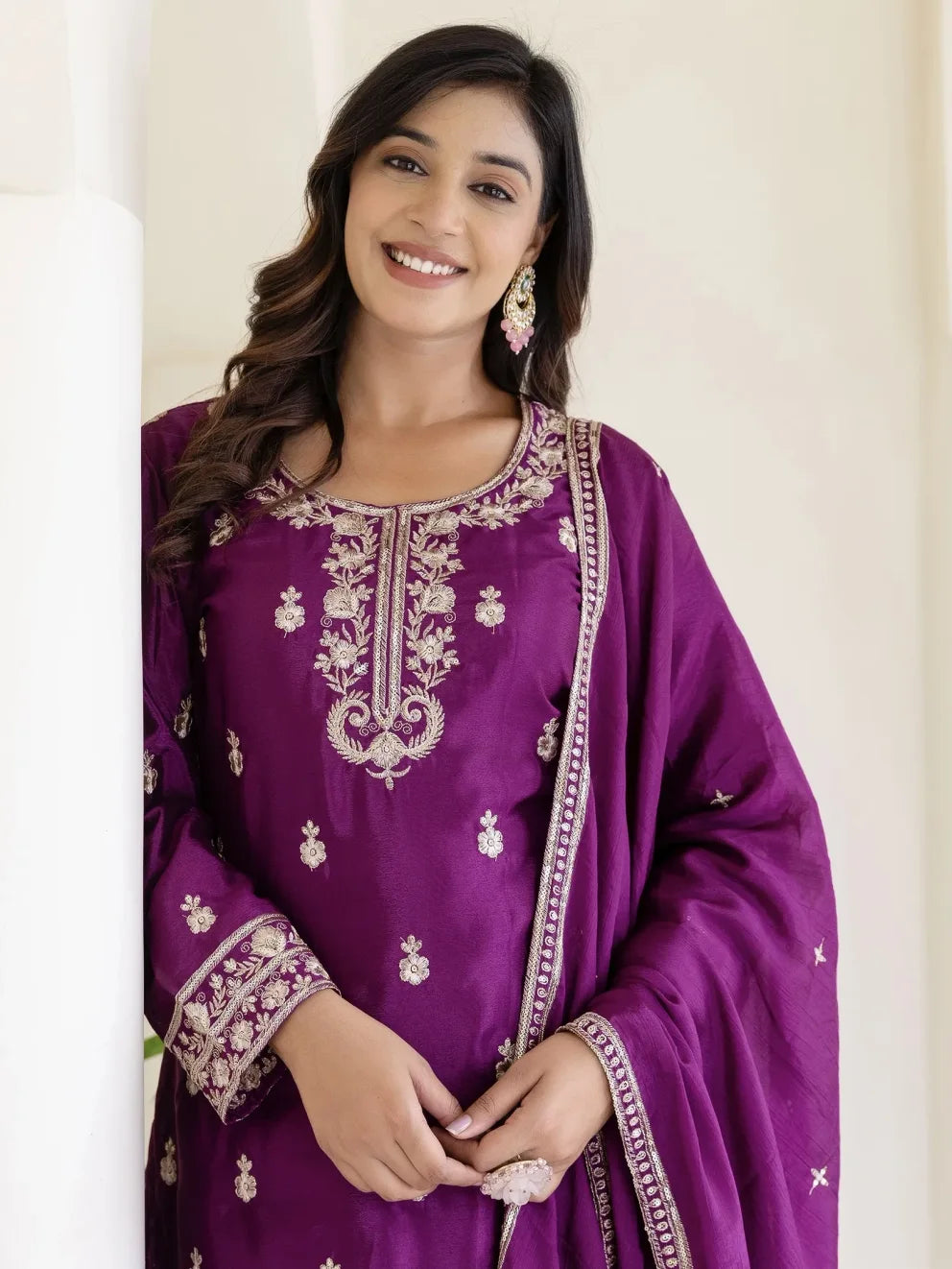 Woman wearing a purple embroidered traditional outfit against a plain background