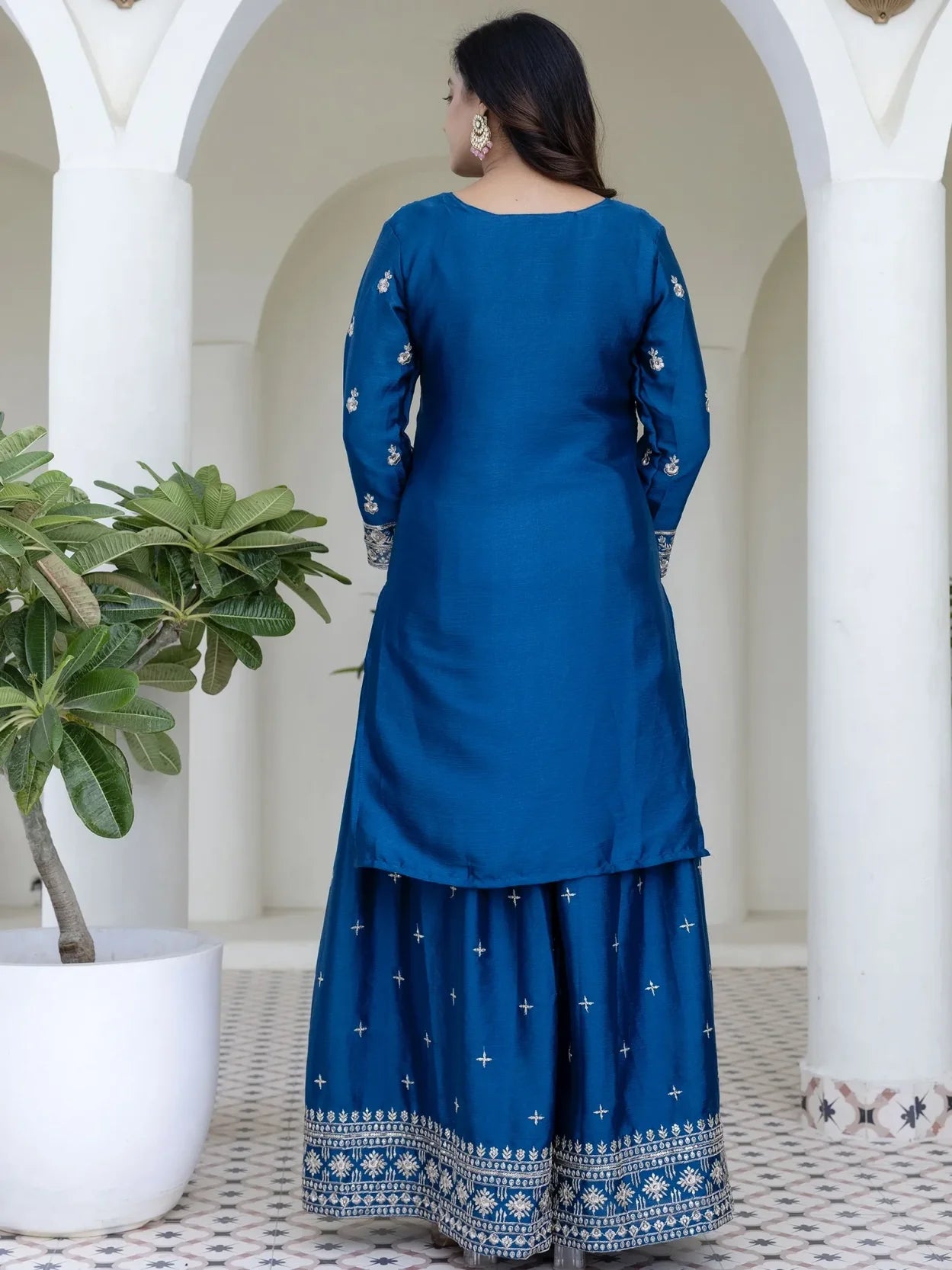 Woman wearing a blue traditional outfit with white patterns in an outdoor setting.