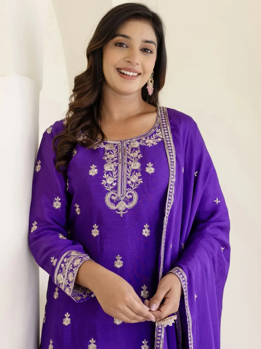 Woman wearing a purple embroidered traditional outfit against a white background