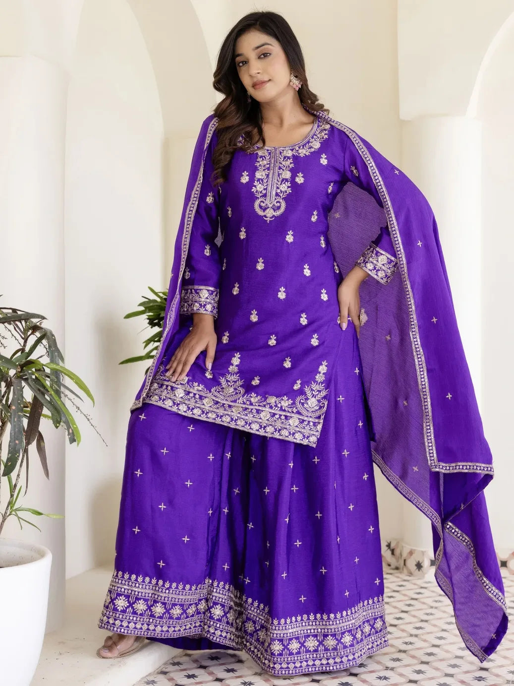 Woman wearing a purple traditional outfit with white embroidery in a minimalistic setting.