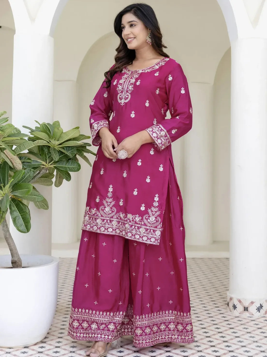 Woman wearing a pink traditional outfit with white embroidery in an indoor setting.