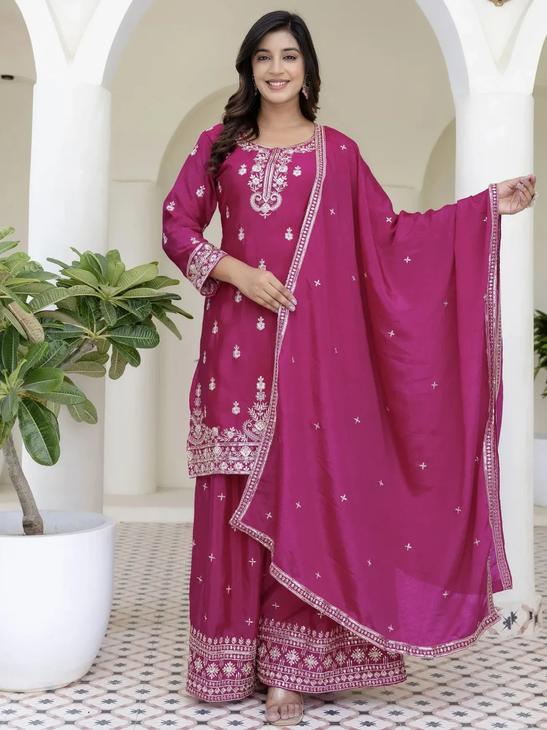 Woman wearing a pink traditional outfit with white embroidery in an outdoor setting.