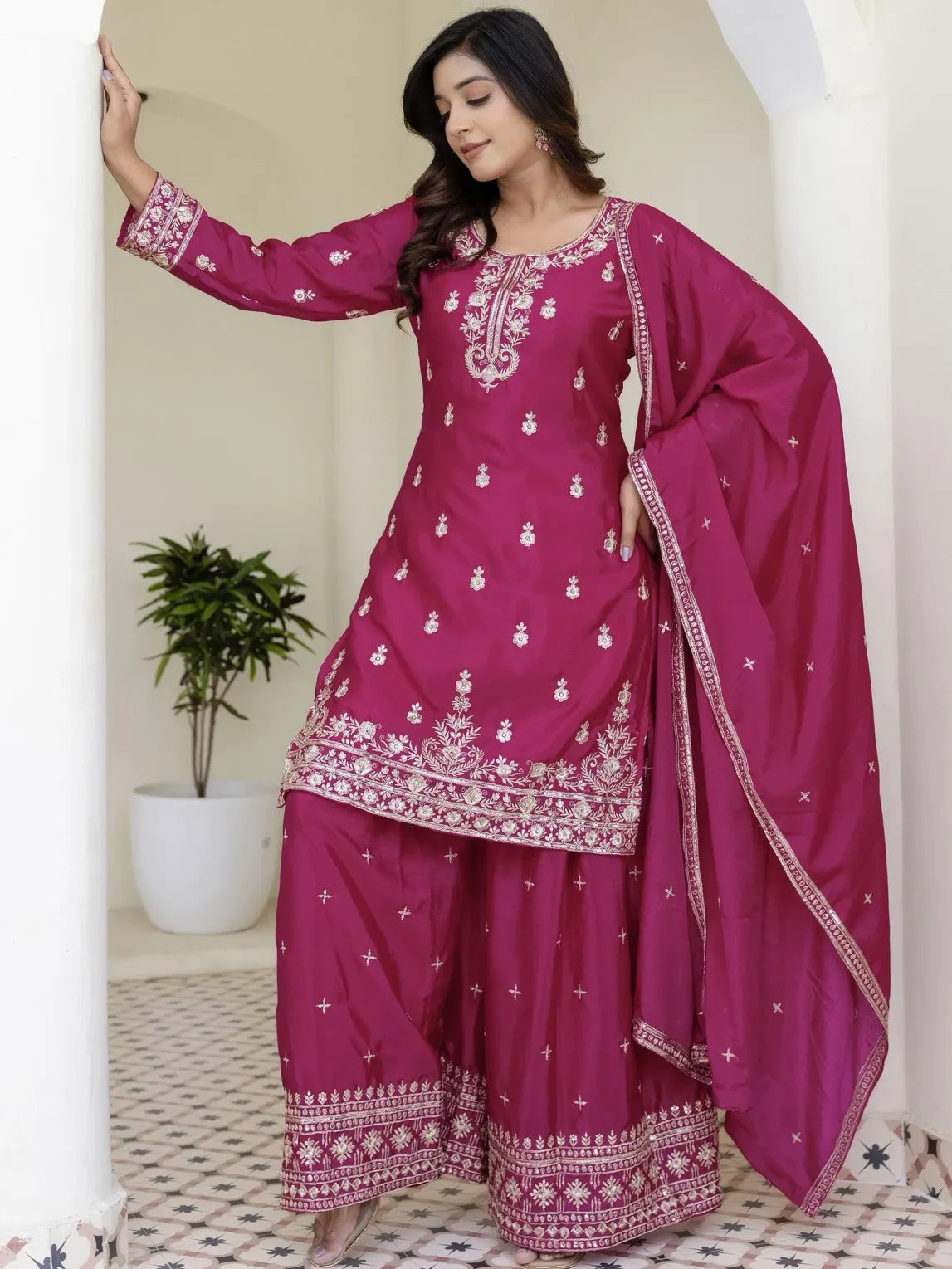 Woman wearing a pink traditional outfit with white embroidery in a minimal indoor setting.