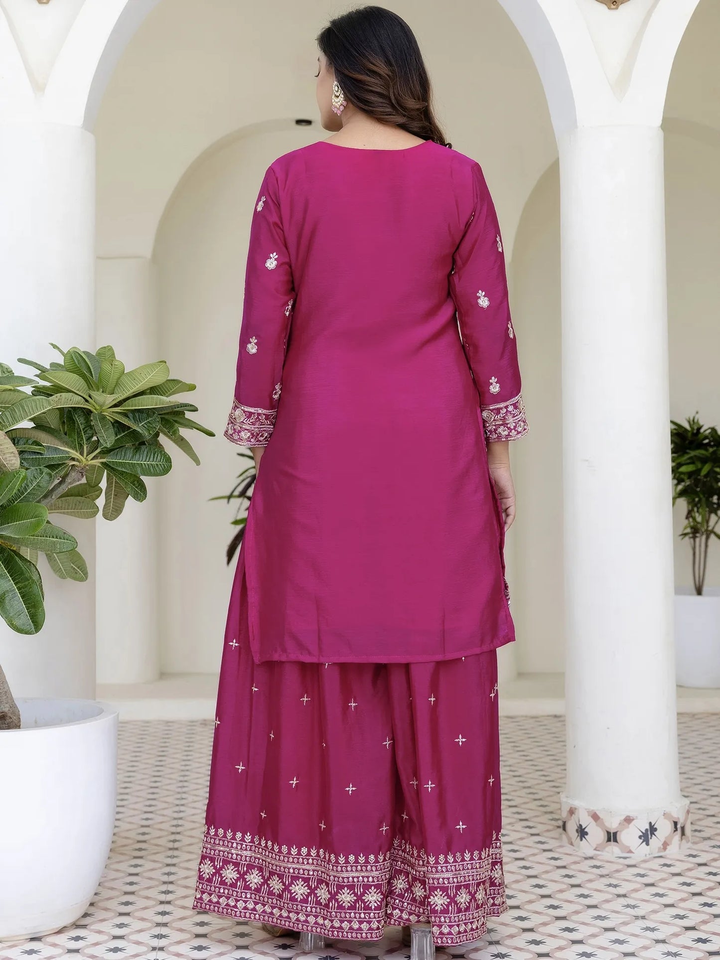 Woman wearing a magenta traditional outfit with white patterns in an outdoor setting.