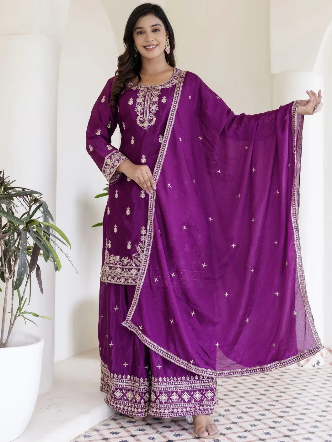 Woman wearing a purple embroidered traditional outfit with a matching dupatta in a minimalistic setting.