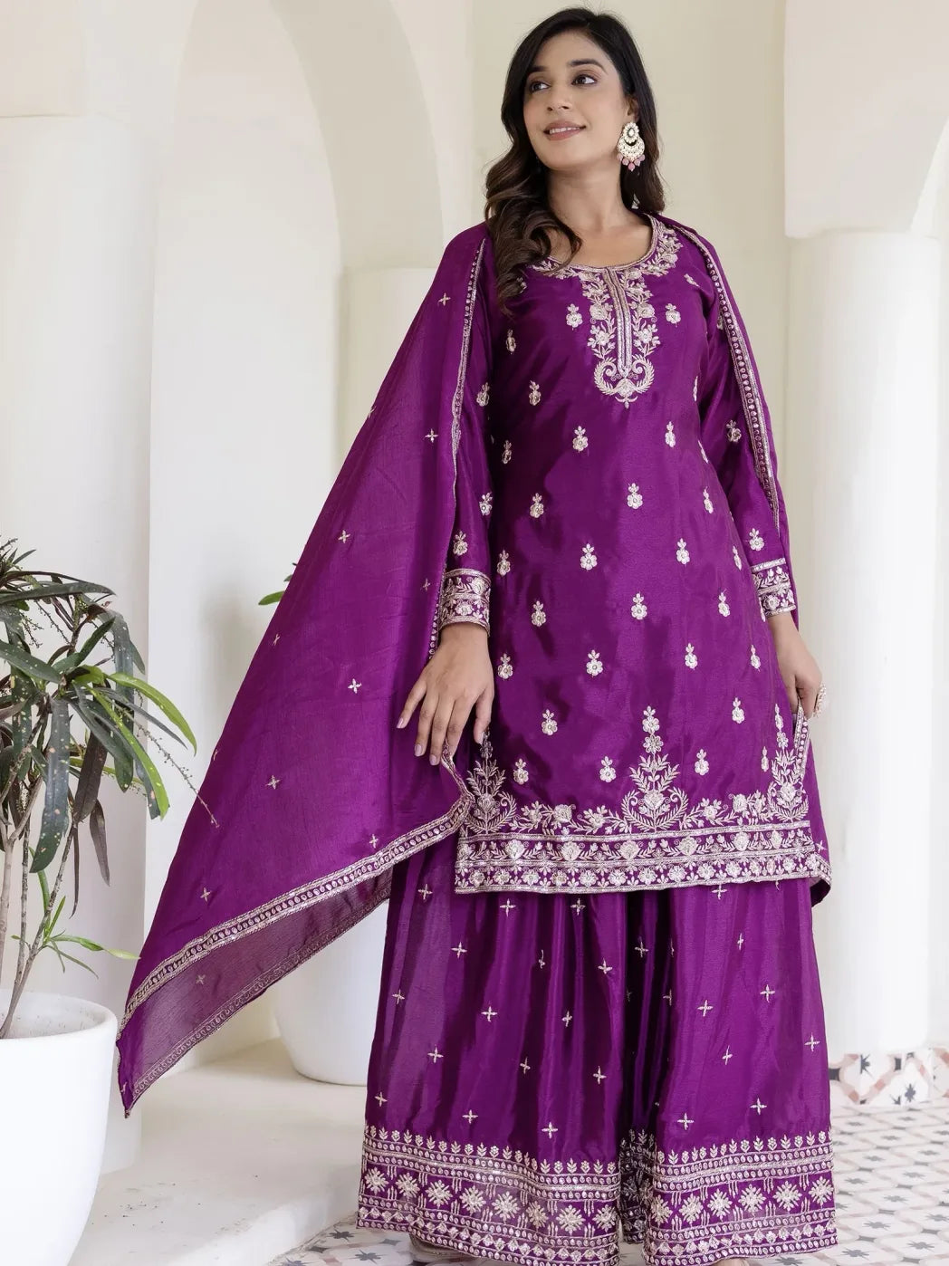 Woman wearing a purple traditional outfit with white embroidery in a minimalistic setting.