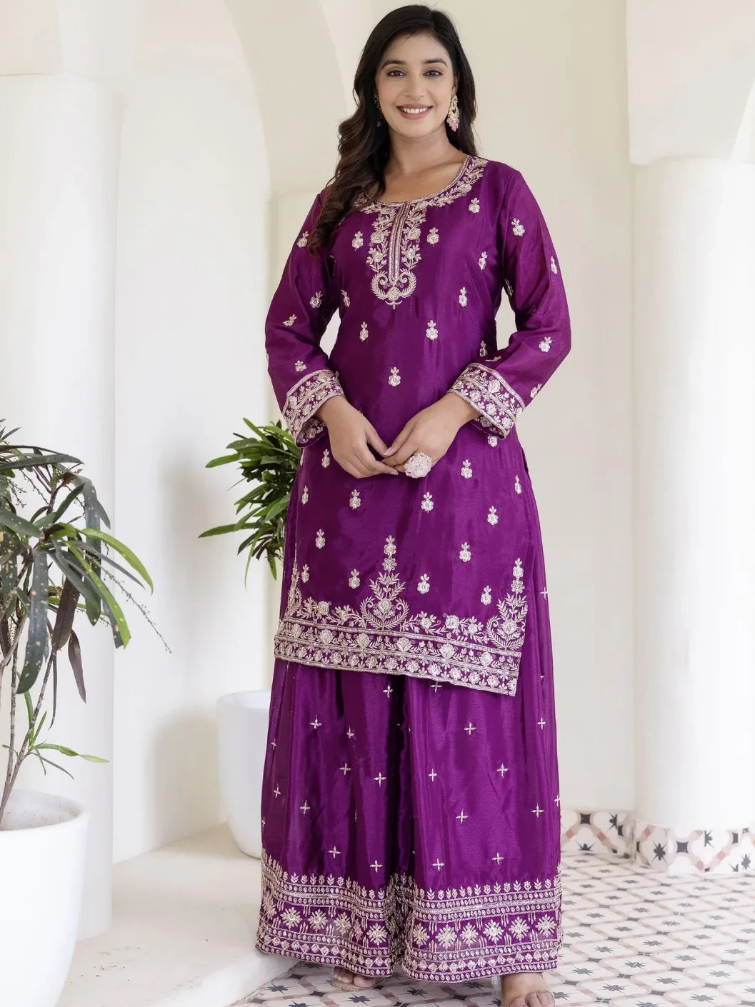 Woman wearing a purple traditional outfit with white patterns in a minimalistic setting.