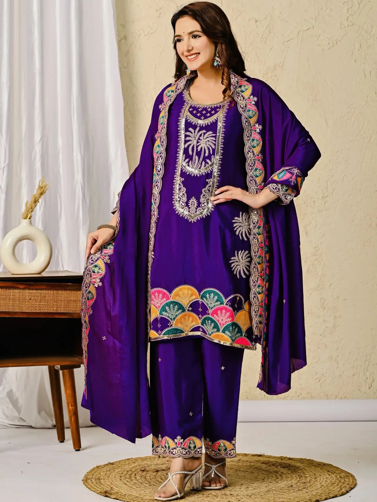 Woman wearing a purple embroidered outfit with a colorful shawl indoors.
