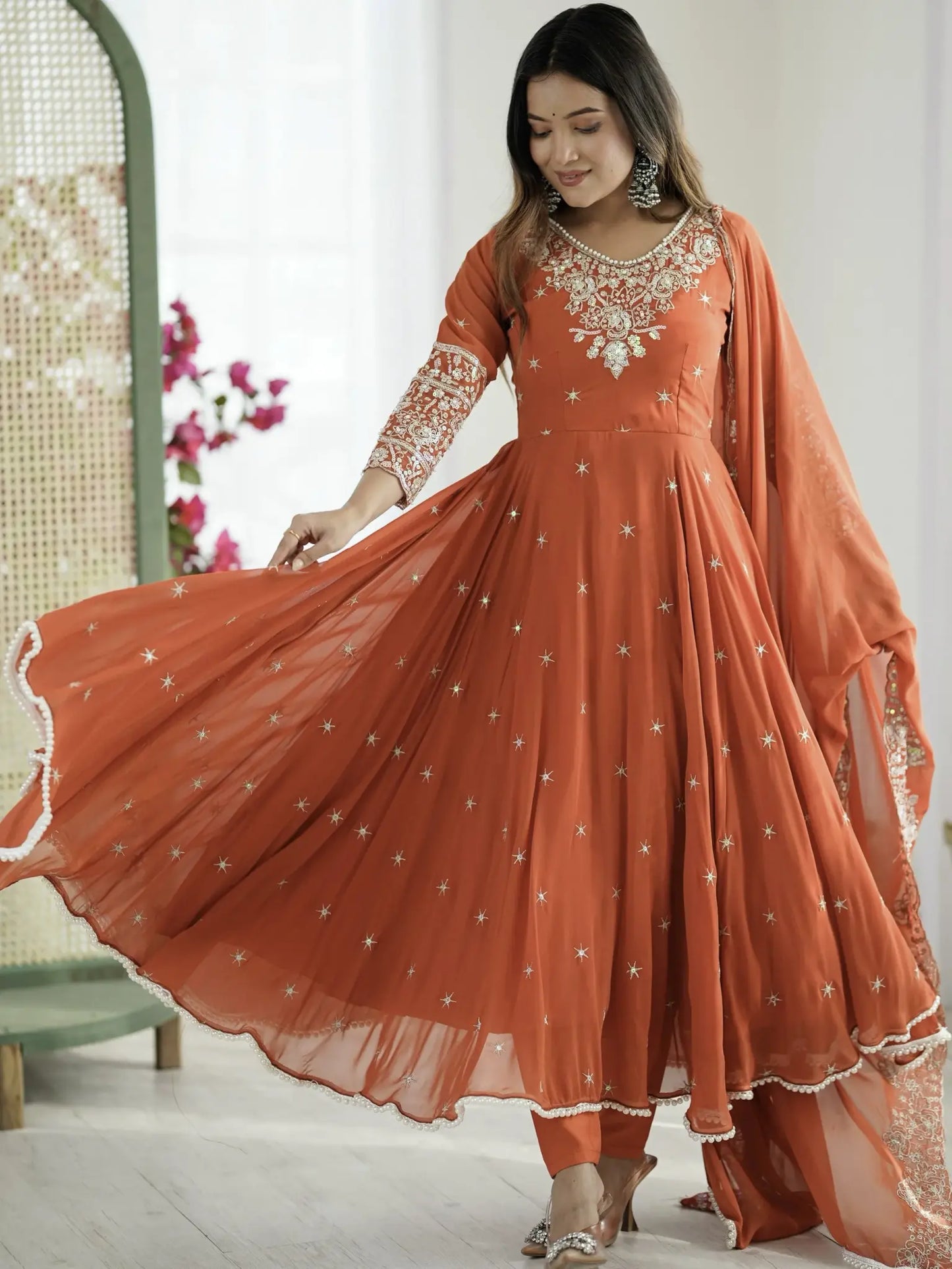 Woman wearing an orange traditional outfit with white embroidery in a bright room.