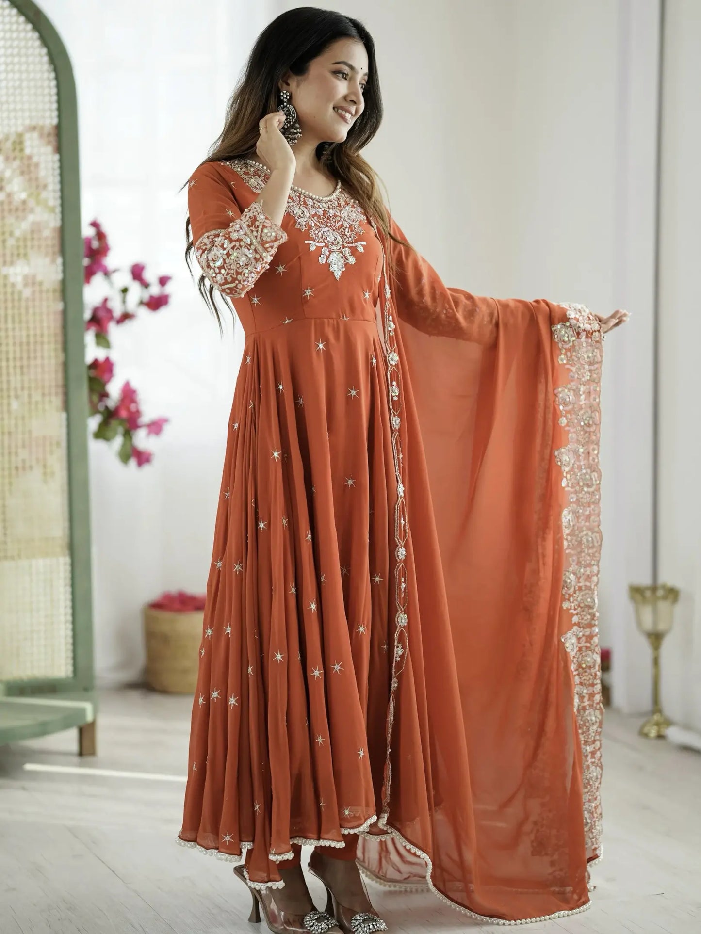 Woman wearing a rust-colored embroidered dress with a matching dupatta in a bright room.