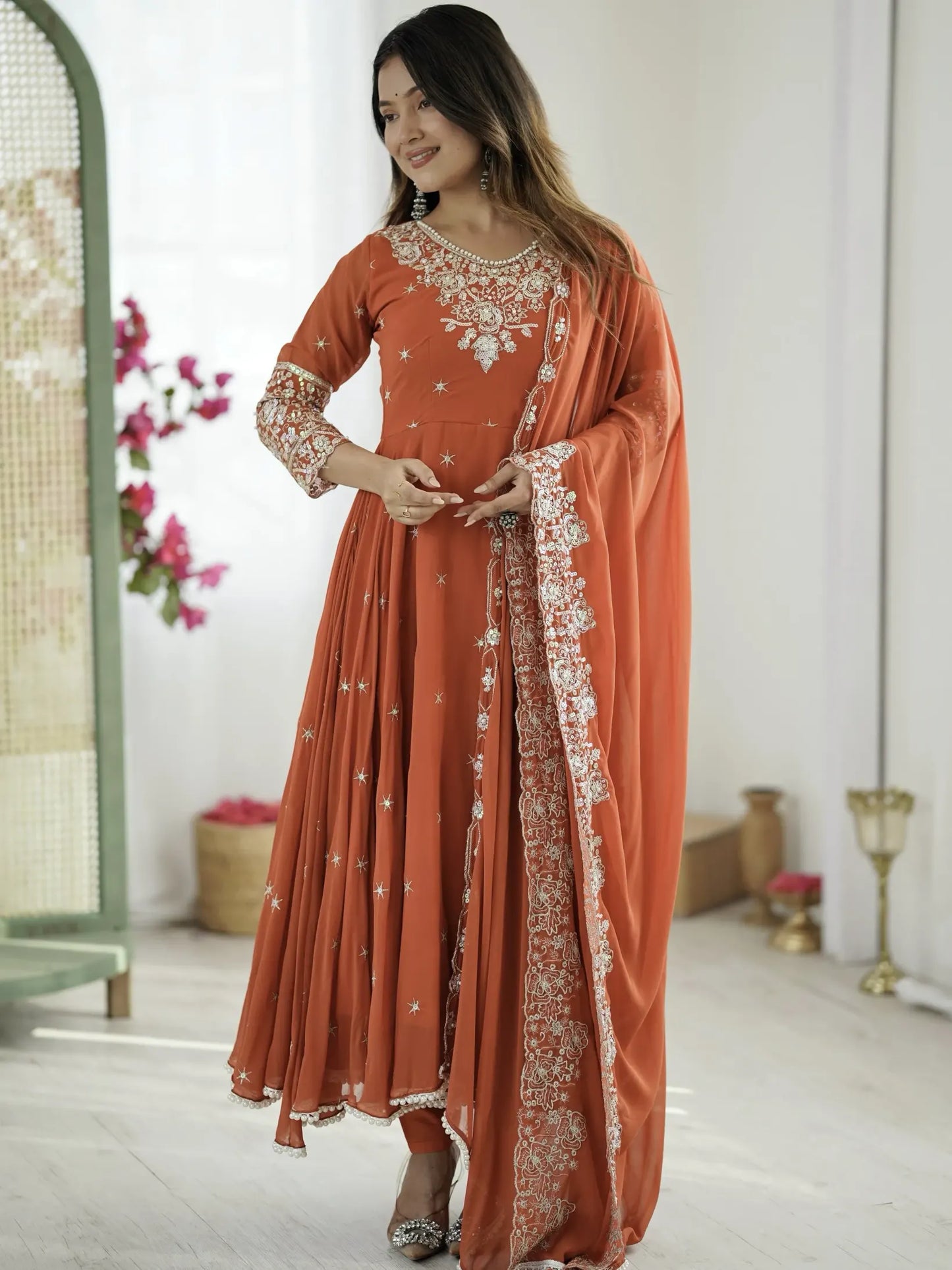 Woman wearing an orange traditional outfit with white embroidery in a minimalistic setting.