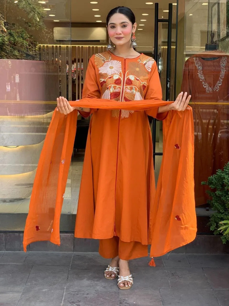 Woman holding an orange dupatta in front of a store entrance