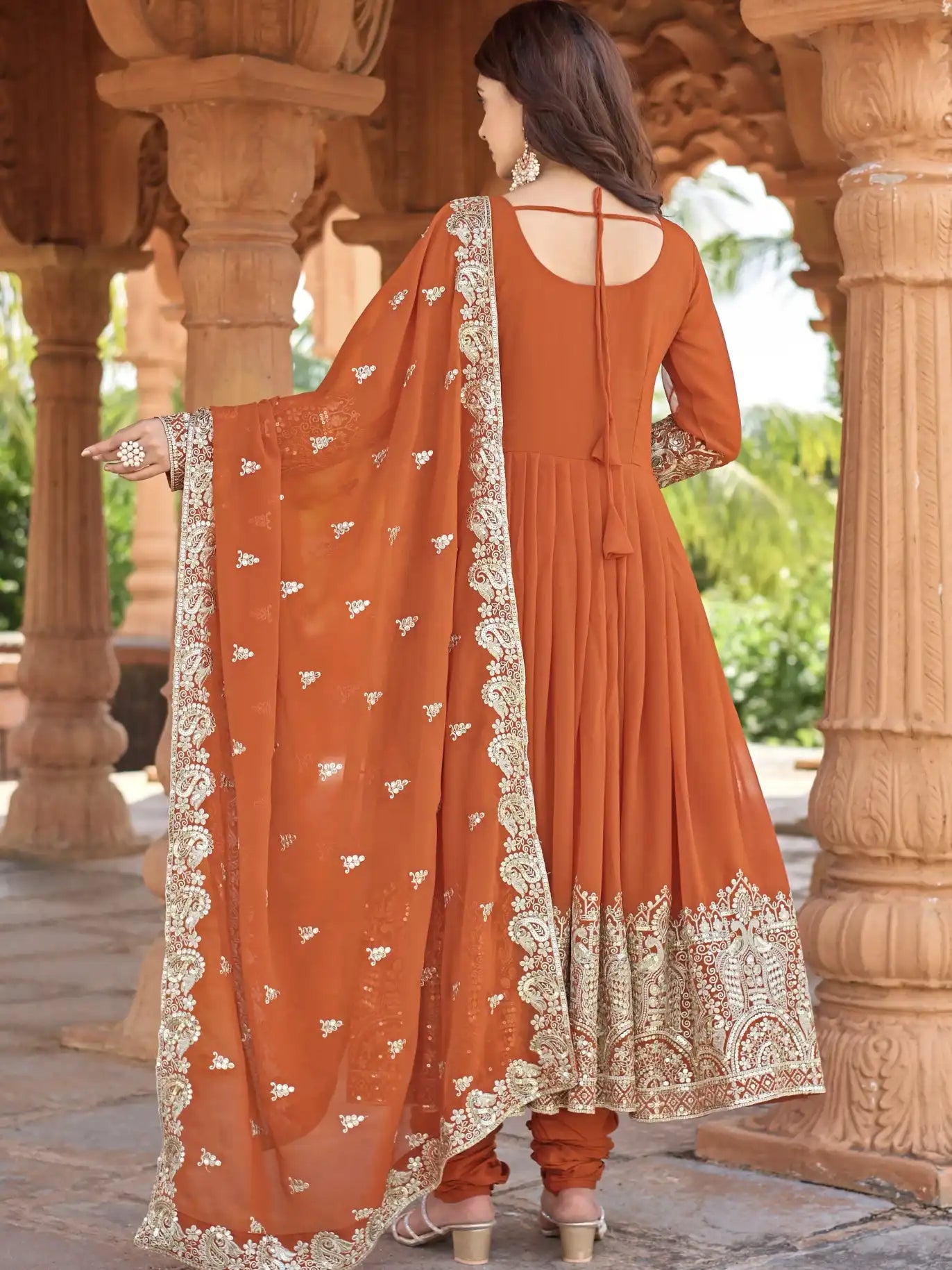 Woman wearing an orange traditional outfit with intricate patterns in a scenic setting.