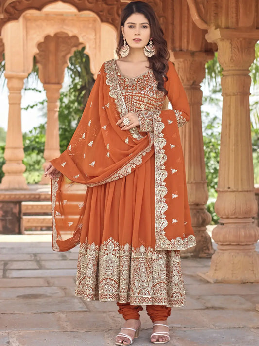 Woman wearing an orange traditional outfit with intricate patterns in a decorative setting.