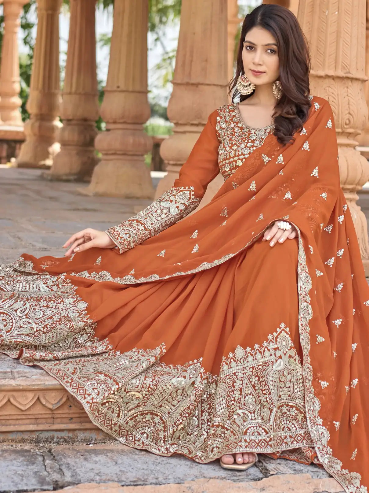 Woman in an orange embroidered traditional outfit sitting outdoors.