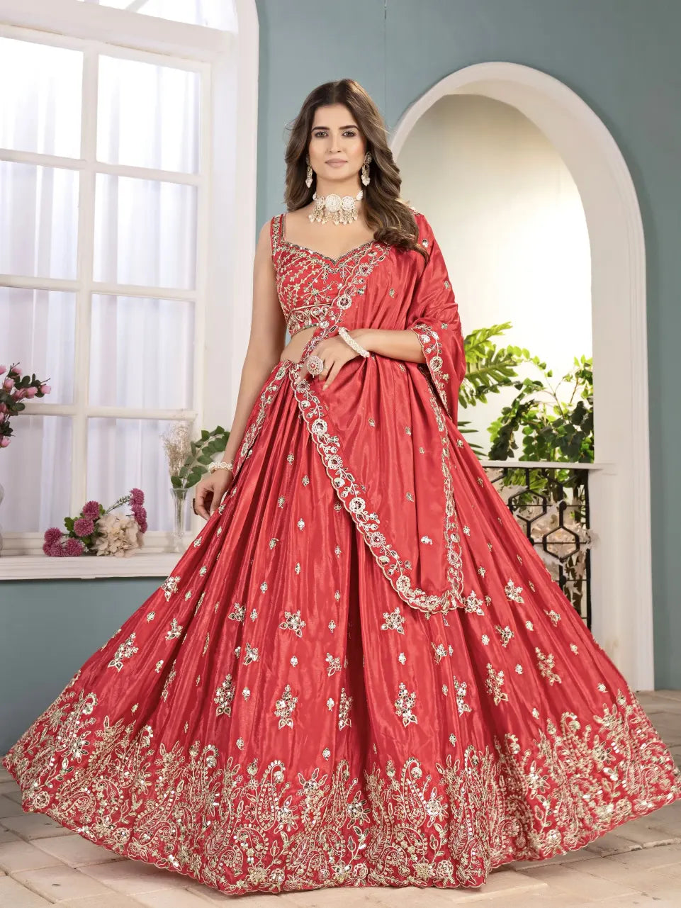 Woman in a red embroidered traditional gown standing indoors with a decorative background.