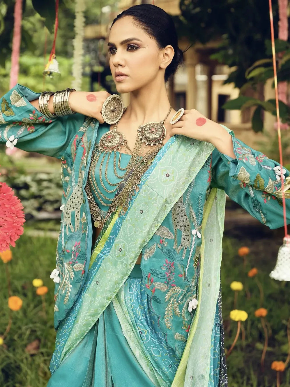 Woman in a traditional turquoise saree with floral patterns in an outdoor setting.