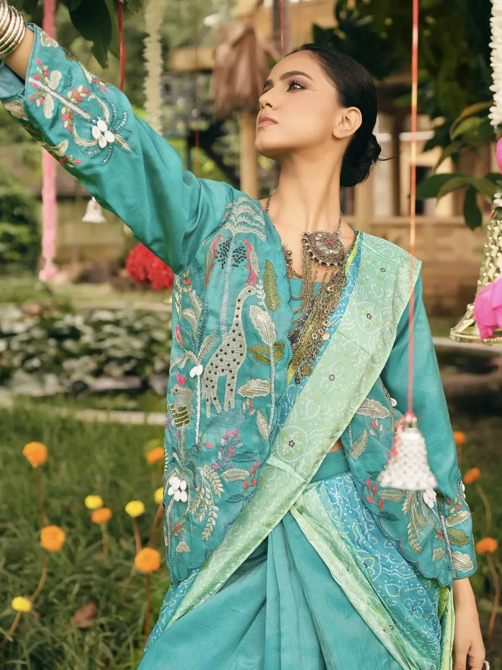 Woman in a traditional turquoise embroidered saree with a floral background