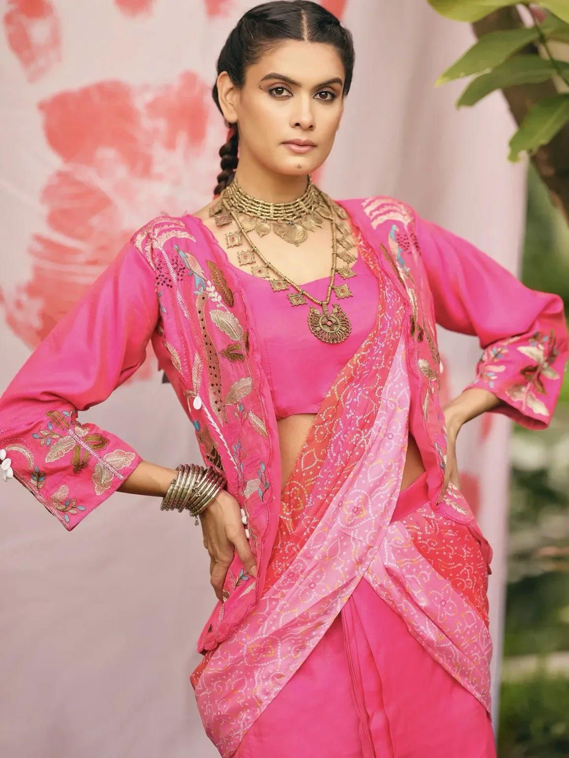 Woman in a pink saree with gold embroidery against a floral background